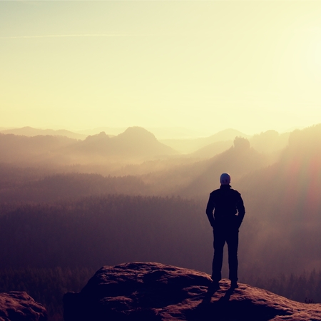 Slim tourist on the sharp peak of rock in rock empires park  is watching over the misty and foggy morning valley to Sunの写真素材