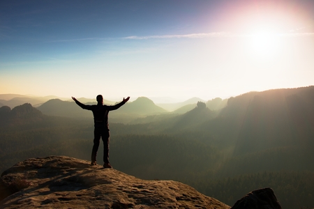 Hiker in black. Gesture of triumph. Tall tourist on the peak of sandstone rock in national park Saxony Switzerland watching down to landscape.の写真素材