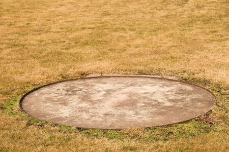 Concrete manhole cover drainage system in the midst of cropped grassの写真素材