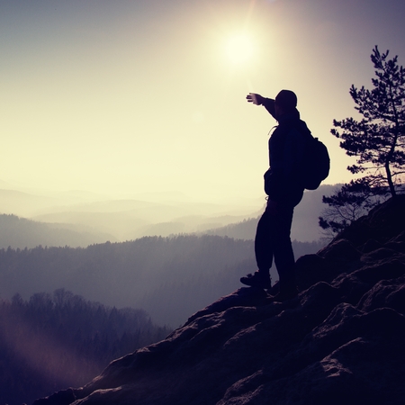 Sunny morning. Hiker is standing on the peak of rock in rock empires park and watching over the misty and foggy morning valley to Sun.の写真素材