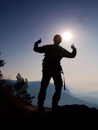 Happy man gesture of triumph. Funny hiker on the peak of sandstone rock in national park Saxony Switzerland watching into camera, the Sun behind head.の写真素材