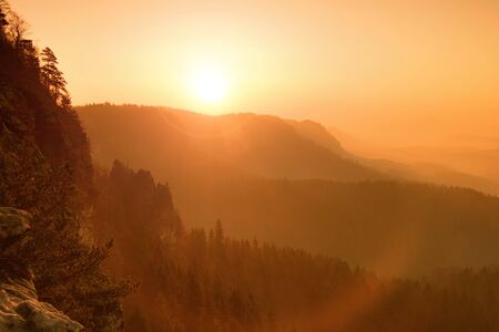 Dreamy fogy landscape, gentle orange misty sunrise in a beautiful valley of Saxony Switzerland park. Sharp hill increased from fog.の写真素材