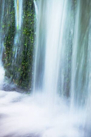 Small waterfall on small mountain stream, mossy sandstone block. Clear water is hurry jumping down into small pool.の写真素材