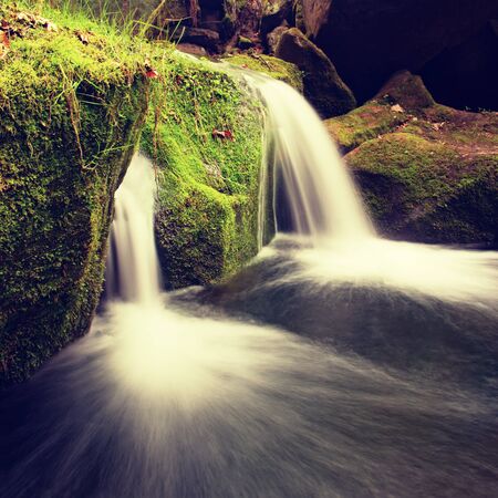 Cascade on small mountain stream. Cold crystal  water is falling over mossy boulders into small pool.の写真素材