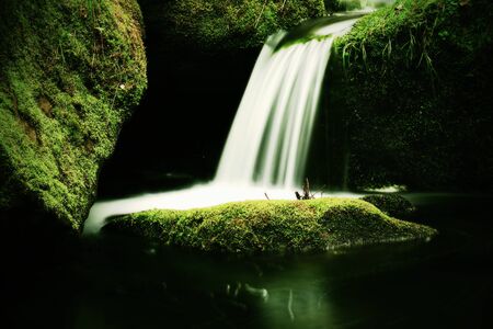 Cascade on small mountain stream. Cold crystal  water is falling over mossy boulders into small pool.の写真素材