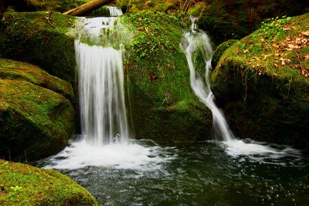 Cascade on small mountain stream. Cold crystal  water is falling over mossy boulders into small pool.の写真素材