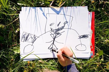 Close up view of child's hand drawing colorful ornaments on paper. Notebook in fresh grass of meadow.の写真素材
