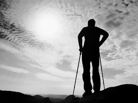 Tall backpacker with poles in hand. Sunny spring daybreak in the Rocky Mountains. Hiker with big backpack stand on rocky view point above the misty valley.の写真素材