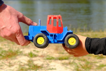 Father's large hand pass plastic toy truck to hand of a boy. Hands in blue and black shirts.の写真素材