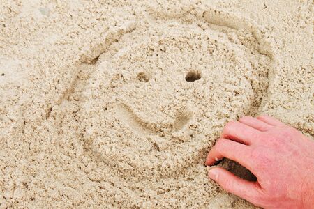Hand paint smiley face in summer beach sandの写真素材