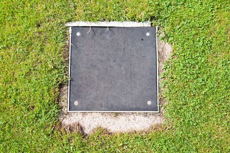 Metal manhole square cover drainage system in the midst of cropped grassの写真素材