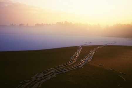 Snowy trails dressed in a blanket of snowy ice on lake. Frozen water level in the misty freeze winter evening.の写真素材