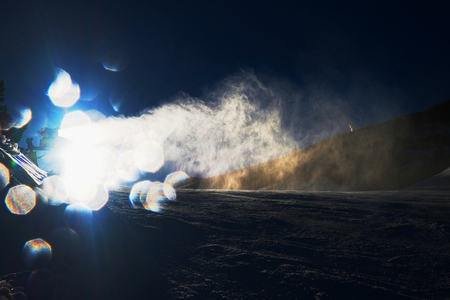 Snowmaking on slope. Skier near a snow cannon making fresch powder snow. Mountain ski resort and winter calm mountain landscape.の写真素材