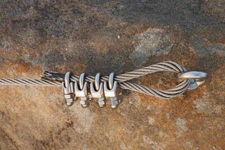 Solid knot on steel rope. Iron twisted rope fixed in block by strong  screws snap hooks. Detail of rope end anchored into rocky wallの写真素材