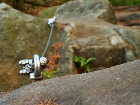 Iron twisted rope streched between rocks in climbers patch.  Rope fixed in block by screws snap hooks. Detail of rope end anchored into sandstone rockの写真素材