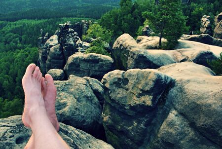 Naked male sweaty legs on peak of rock above valley.