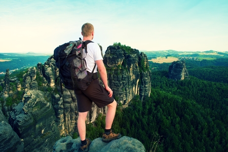 Tall tourist with big backpack. Sunny evening in rocky mountains of Saxony Switzerland park. Hiker stand on rocky view point above valley.の写真素材