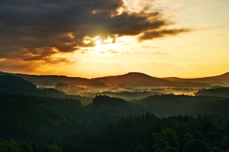 lighted rocks and hills bellow sunset sun on  horizon. Dark forestの写真素材
