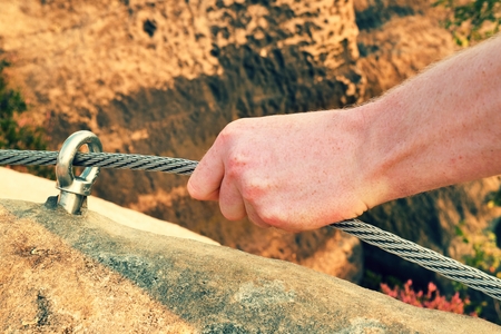 Rock climber's hand hold on steel twisted rope at steel bolt eye anchored in sandstone rock. Tourist path via ferrata.の写真素材