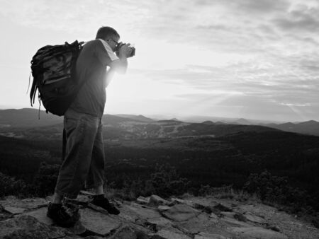 Professional photographer with big mirror camera on neck on peak of rock. Hilly landscape, spring...