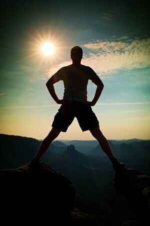 Jumping hiker in black gesture triumph between two rocky peaks. Wonderful daybreak.の写真素材