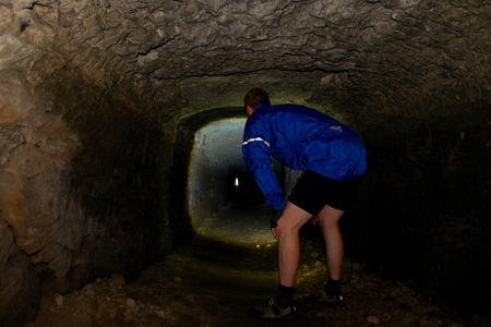 Boy hiker - mountainbiker in a sabdstone cave or dry water channel, back shot. Visiting of undergroundの写真素材