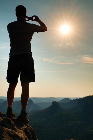 Hiker with taking photo by smart phone on the peak of mountain at sunrise.の写真素材