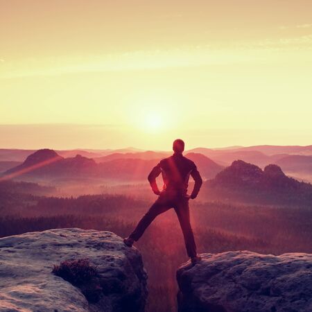 Jumping hiker in black celebrate triumph between two rocky peaks. Wonderful daybreak.の写真素材