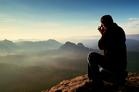 Dark hair man is taking photo by  big mirror camera on the neck on the peak of mountainsの写真素材
