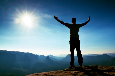 Man gesture triumph. Happy hiker in black. Tall man on the peak of sandstone rock in national park Saxony Switzerland watching down to landscape.の写真素材