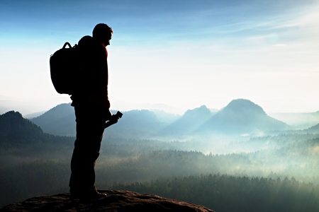 Silhouette of photographer overlooking a blanket of fog over valley to sunの写真素材