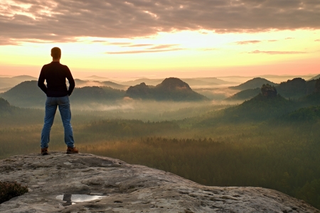 Hiker is standing on the peak of sandstone rock in rock empires park and watching over the misty and foggy morning valley to Sun. Beautiful moment the miracle of natureの写真素材