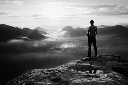 Hiker in red cap stand on the peak of sandstone rock in rock empires park and watching over the misty and foggy morning valley to Sun. Beautiful moment the miracle of natureの写真素材