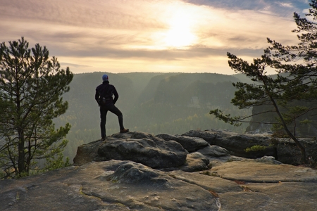 Hiker stand at heather bush on the corner of empire bellow pine tree. Man is watching over the misty and foggy morning's Sun Valleyの写真素材