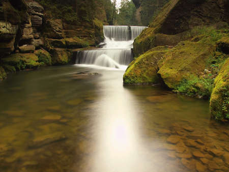 Mountain river with big mossy boulders under fresh green trees. Fresh spring air in the evening after rainy day.の写真素材
