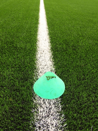 Bright green blue plastic cone on white painted line. Plastic green turf football playground with...
