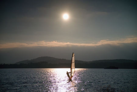 Windsurfer leans back into breeze Shot with gentle filter. Strong sun makes reflections in mirror of water level.の写真素材