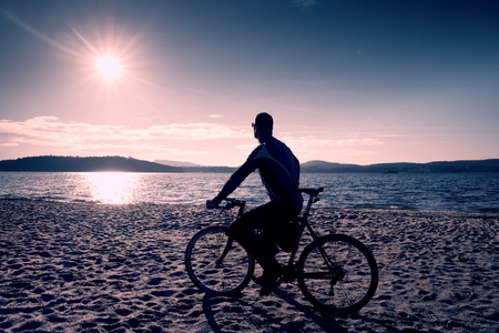 Young man cyclist sit on bike,  blue sky and sunset background on beach. End of season at lake and popular tourist resort..の写真素材