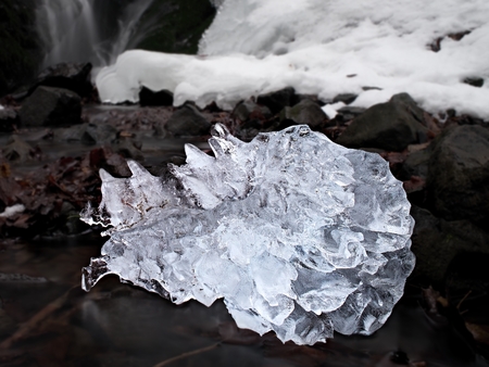 Beautiful big piece of ice with abstract cracks inside. Fallen icicle bellow waterfall, stony and...