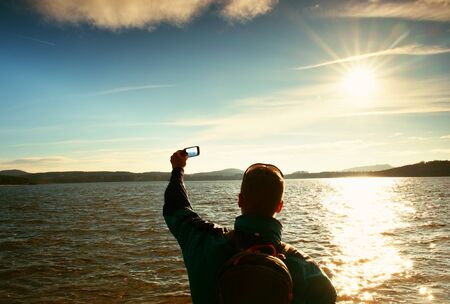 Tall ginger hair man tourist taking photos or video with mobile phone. Autumn sunny day at sea...