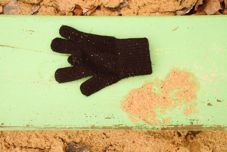 Lost woolen gloves on green bench. Sandy wooden bench. Sandbox with dirty sand in kinder garden. Wooden bench.の写真素材