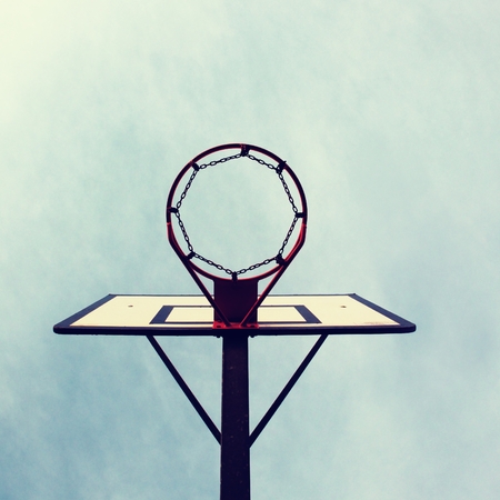 Old neglect basketball backboard with rusty hoop above street court. Blue sky in background.