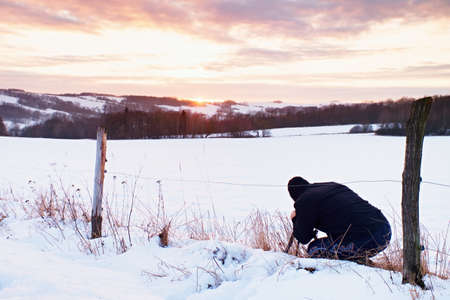 Photographer lay in snow on meadow and takes a picture of fantastic sunset above opposite hillの写真素材