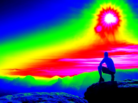 Man on rock. Fantastic infrared scan. Tourist on the rocky peak. Daybreak in mountains, heavy mist in deep valley in colors of ultra violet measurementの写真素材