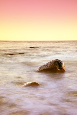 Romantic morning at sea. Big boulders sticking out from smooth wavy sea. Long exposure for smooth dreamy water level.の写真素材