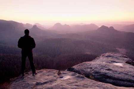 Tall man in black on cliff and watch to mountain sunrise.Silhouette in selfconfident pose.  Dark silhouette of rocks.の写真素材
