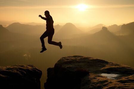 Crazy hiker in black is jumping between rocky peaks. Happy man. Wonderful daybreak in rocky...