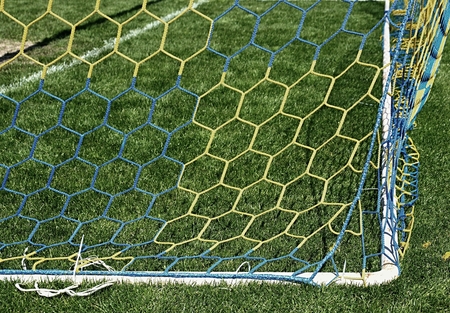 Hang bended blue yellow soccer nets, soccer football net. Grass on football playground in the backgroundの写真素材