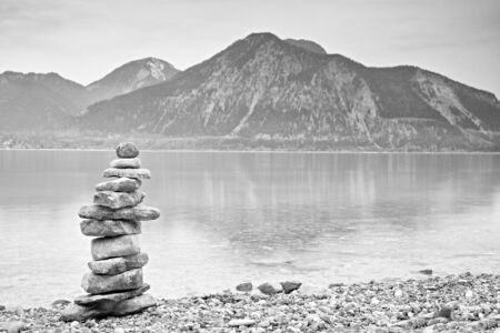 Balanced stone pyramide on shore of blue water of mountain lake. Blue mountains in water level...