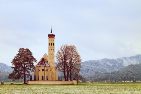 Old church with high bell tower and graveyard bellow mountains.  April weather. Wet spring snow in already fresh green grass  of meadow bellow mountains.の写真素材